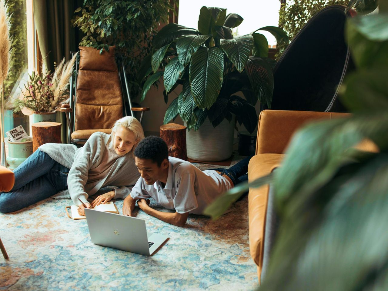 Two people lying on a rug at home, both looking at a laptop screen
